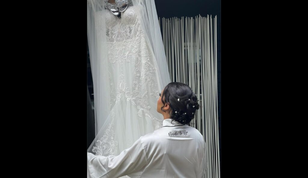 Bride admiring her lace wedding gown hanging in a doorway before storage