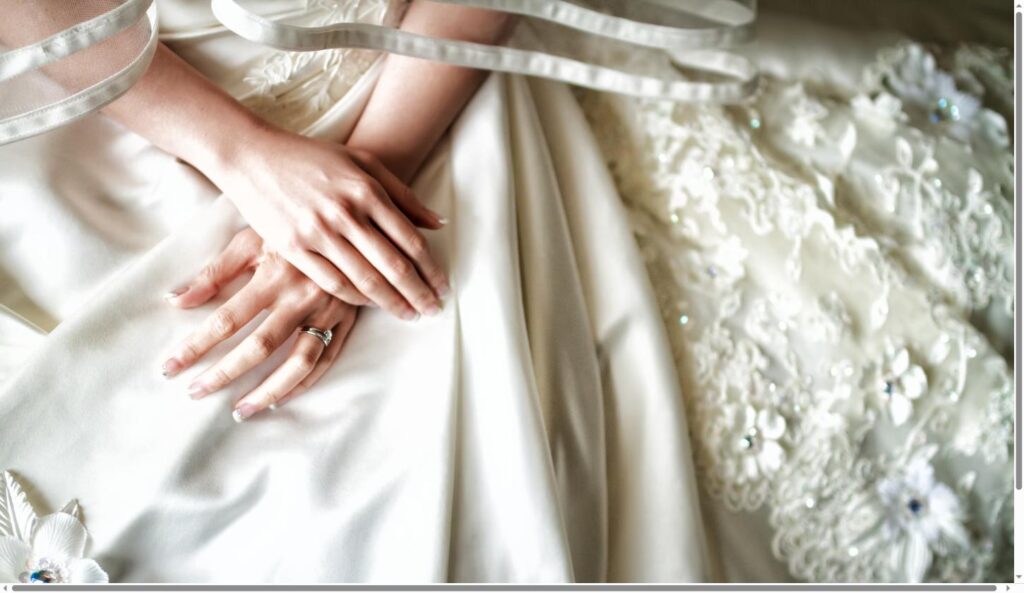 Bride's hands resting on satin fabric with lace wedding dress detail
