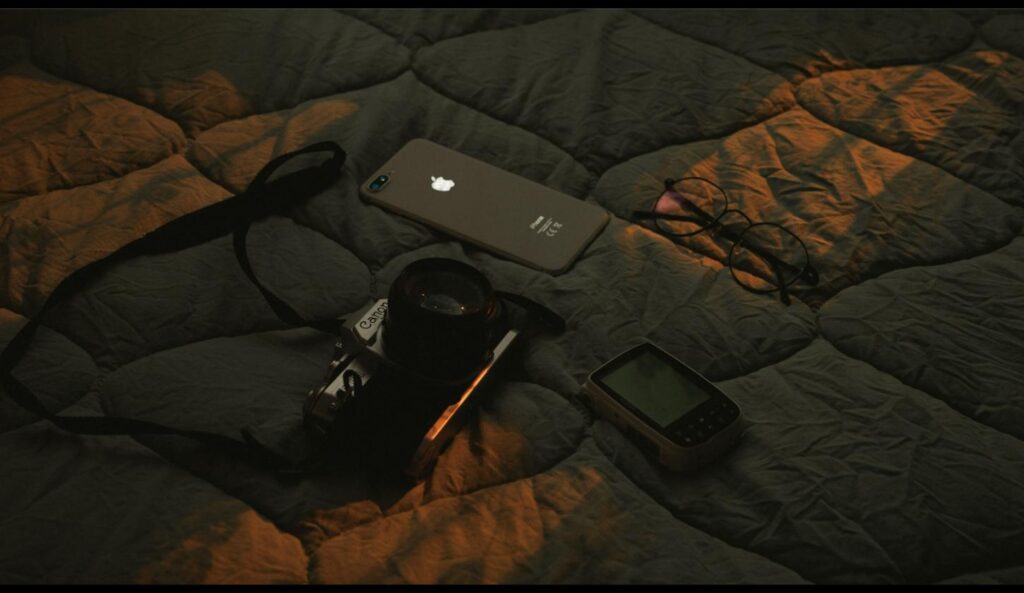 iPhone lying flat on a bed beside a vintage camera and eyeglasses