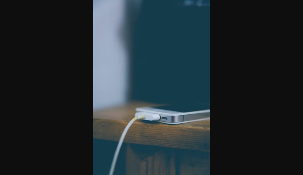 Silver iPhone charging with a Lightning cable on a wooden desk