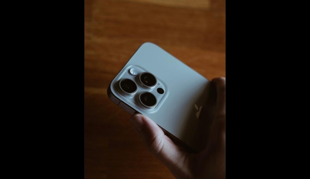 Hand holding an iPhone showing its triple camera lens close up
