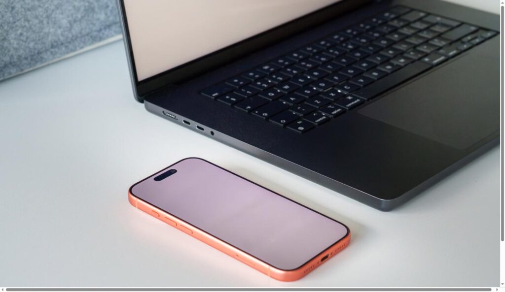An iPhone resting on a desk next to an open MacBook
